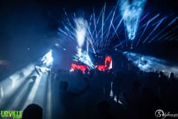 Foule du Festival d'Urville devant la scène principale, lumières lasers bleues, ambiance électro nocturne